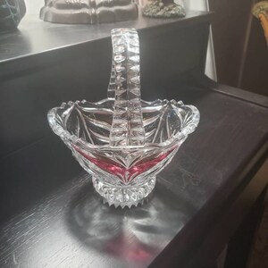 Peut inclure: Un panier en verre transparent avec une bordure rouge et une poignée en cristal. Le panier est posé sur une surface noire.