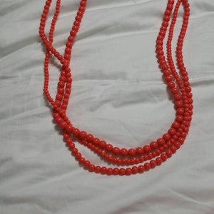 May include: A multi-strand necklace made of bright orange beads. The necklace has a silver clasp.