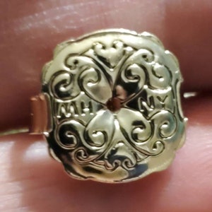May include: Gold-toned metal ring with an ornate design featuring a central circle and the letters "MH" and "NY" on either side.
