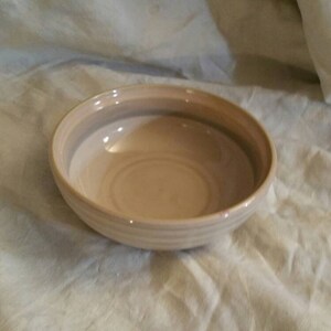 May include: A white ceramic bowl with brown stripes. The bowl is empty and sitting on a white surface.