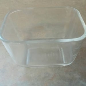 Op de afbeelding: Een vierkante glazen container met afgeronde randen.