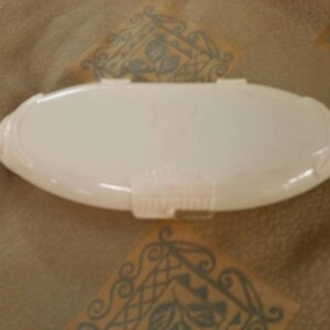 May include: A white oval-shaped plastic container with a hinged lid. The container is empty and has a smooth surface.