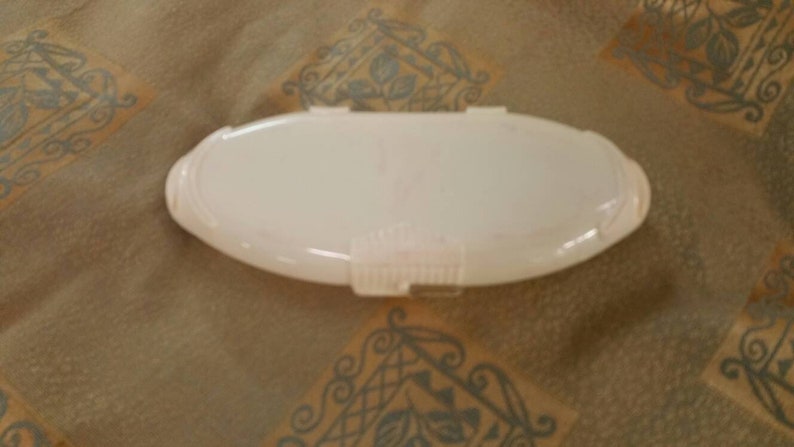 May include: A white oval-shaped plastic container with a hinged lid. The container is empty and has a smooth surface.