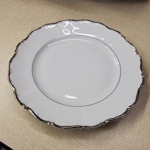 Könnte beinhalten: Weiße Keramik-Dinnerplatte mit silbernem Rand und gewelltem Rand.