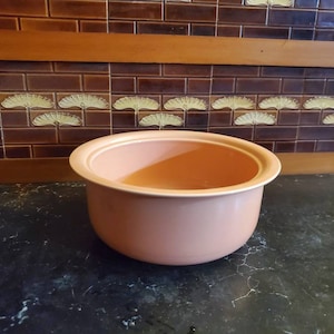 Op de afbeelding: Een grote, perzikkleurige keramische kom met een licht afgeronde rand. De kom staat op een zwart oppervlak.