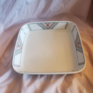 Puede incluir: Un plato para hornear de cerámica blanca con un patrón geométrico en tonos de verde, marrón y rosa alrededor del borde.