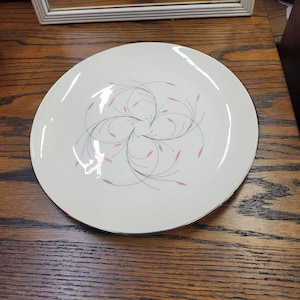 May include: A white ceramic plate with a black and pink floral design. The plate has a black rim and is on a wooden surface.