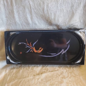 May include: A black oval tray with a raised rim and a painted design of a stylised bird with orange, purple, and white accents. The tray is in a box.