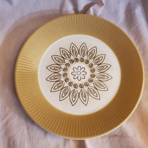 May include: A yellow ceramic dinner plate with a brown floral design in the centre. The plate has a fluted edge.