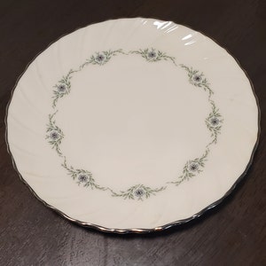 May include: A white ceramic plate with a silver rim and a delicate floral design in green and blue.
