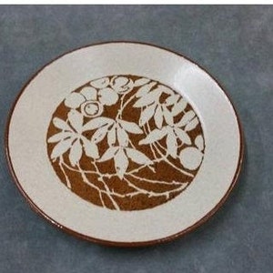 May include: A white ceramic plate with a brown floral design. The design features leaves and berries in a circular pattern.