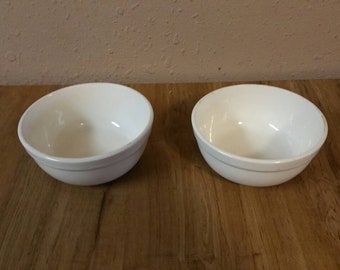 May include: Two white ceramic bowls on a wooden surface. The bowls are empty and have a simple design.