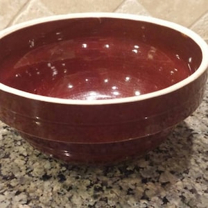 May include: A brown ceramic mixing bowl with a white rim. The bowl has a slightly rounded bottom and is made of a thick, durable material.