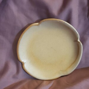 May include: A small, scalloped, light yellow ceramic plate with a slightly textured surface.
