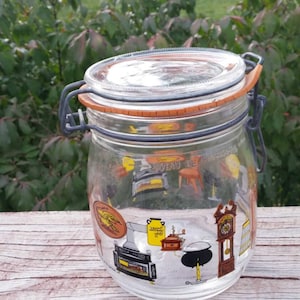 May include: A clear glass jar with a metal lid and a rubber seal. The jar has a vintage design with a colorful illustration of a stove, a clock, and other kitchen items.
