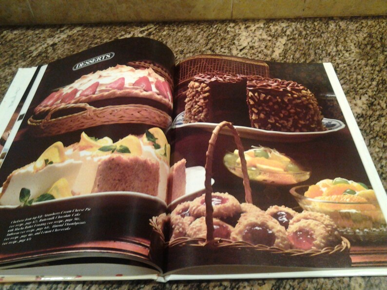 Puede incluir: Libro de cocina abierto con una variedad de recetas de postres, que incluyen una tarta de merengue de fresa, un pastel de chocolate con nueces, una tarta de crema de lim&oacute;n y galletas con relleno de mermelada. El libro tiene la palabra "DESSERTS" impresa en la parte superior de la p&aacute;gina.