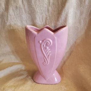 May include: A pink ceramic vase with a decorative floral design. The vase has a wide mouth and a narrow base.