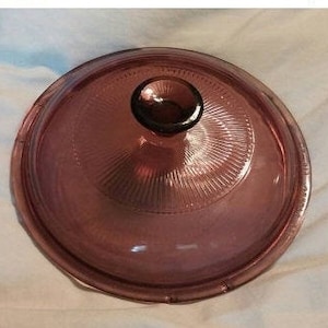 Op de afbeelding: Een paarse glazen deksel met een knop aan de bovenkant. De deksel heeft een getextureerd, geribbeld ontwerp.