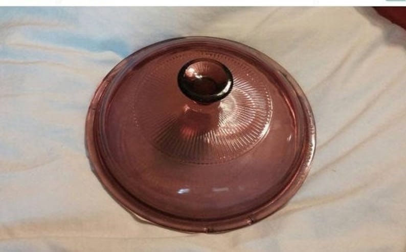 May include: A purple glass lid with a knob on top. The lid has a textured, ribbed design.