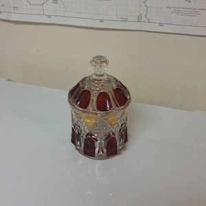 Peut inclure: Un pot à bonbons en verre transparent avec un motif rouge et or. Le pot a un couvercle avec un bouton sur le dessus.