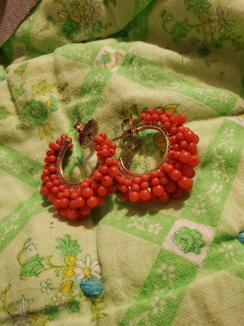 May include: A pair of hoop earrings with a gold base and red beads. The beads are clustered together to form a thick hoop.