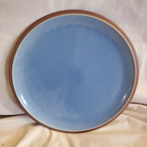 Puede incluir: Un plato de servir grande, redondo, de cerámica azul claro con un borde marrón.