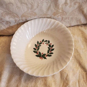 May include: White ceramic bowl with a green holly wreath design. The wreath has red berries and green leaves.