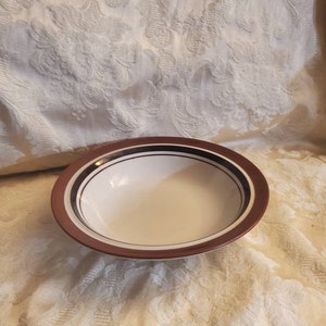 May include: A brown and white ceramic bowl with a wide rim and a simple design. The bowl has a white interior and a brown exterior with a thin white stripe around the top.