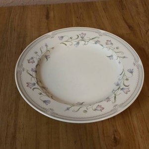 Könnte beinhalten: Ein weißer Keramik-Dinnerteller mit einem Blumendesign mit rosa, lila und grünen Blumen. Der Teller hat einen leicht erhöhten Rand.