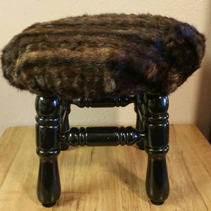 May include: A small black wooden stool with a brown and black faux fur seat.