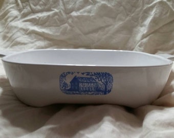 May include: White ceramic baking dish with blue and white design of a house and trees. The dish has two handles on the sides.