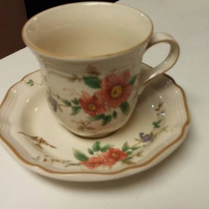 May include: A white teacup and saucer set with a floral pattern. The cup has a handle and the saucer has a scalloped edge.
