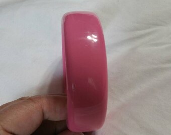 Può includere: Un braccialetto rigido in plastica rosa. Il braccialetto è liscio e lucido.