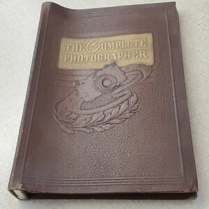 Könnte beinhalten: Ein braunes, ledergebundenes Buch mit dem Titel "The Complete Photographer", der in goldenen Lettern geprägt ist. Der Einband zeigt eine Illustration einer Vintage-Kamera.