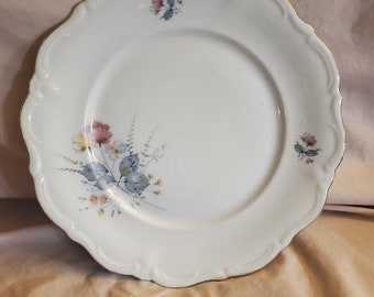 May include: White porcelain dinner plate with a gold rim and a floral design featuring pink, blue, and yellow flowers.