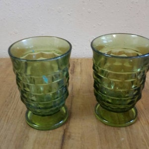 May include: Two green glass tumblers with a diamond pattern and a footed base.