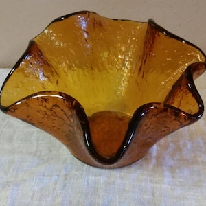 Peut inclure: Un bol en verre brun avec un bord festonné. Le bol a une surface texturée et est fait dans une forme ondulée et organique.