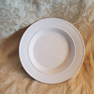 Op de afbeelding: Een wit keramiek bord met een licht verhoogde rand. Het bord heeft een eenvoudig ontwerp en is perfect om een ​​verscheidenheid aan gerechten te serveren.