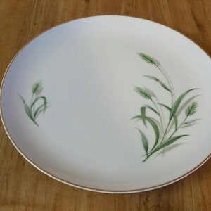 May include: A white, oval-shaped serving platter with a gold rim. The plate features a delicate design of green wheat stalks and leaves. This vintage dish is perfect for serving appetizers or desserts.