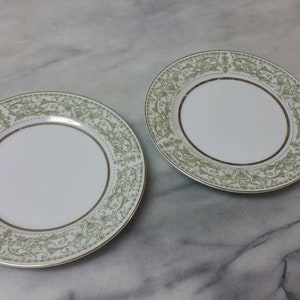 Puede incluir: Dos platos de cerámica blanca con borde dorado y patrón floral verde.