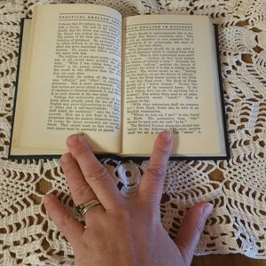 May include: An open book with a blue cover, titled "Practical English for Business" and "Good English in Business". The book is lying open on a white crocheted doily.