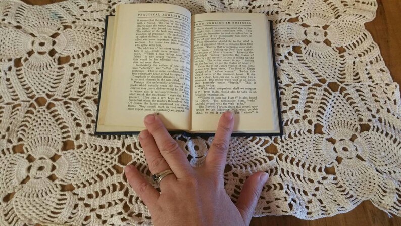 May include: An open book with a blue cover, titled "Practical English for Business" and "Good English in Business". The book is lying open on a white crocheted doily.