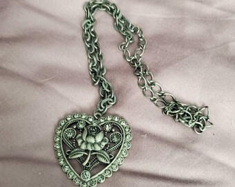 May include: A silver heart-shaped pendant necklace with a rose design and clear rhinestones. The chain is silver and has a link style.