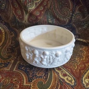 Puede incluir: Tazón de cerámica blanco con un diseño en relieve de querubines alrededor del borde.