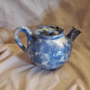 May include: A blue and white ceramic teapot with a speckled glaze. The teapot has a round body and a spout on the side. The lid has a small knob on top.