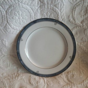 Puede incluir: Un plato de cerámica blanco con un borde azul y dorado. El plato tiene un diseño sencillo con algunos pequeños detalles florales.