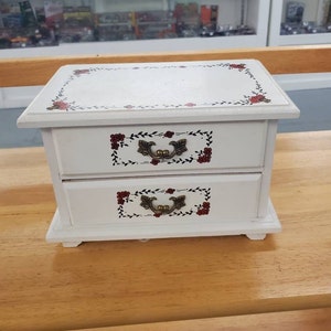 May include: White wooden jewelry box with two drawers. The drawers have floral designs with red flowers and gold handles.