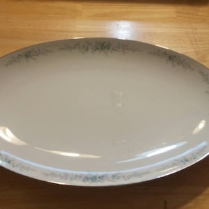 Op de afbeelding: Witte ovale serveerschaal met een zilveren rand en een delicaat blauw bloemenpatroon.