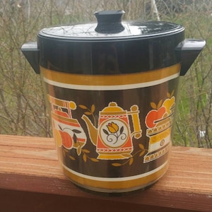 May include: A black and gold ice bucket with a retro design featuring a teapot, a stove, and fruit. The bucket has a black lid with a knob on top.