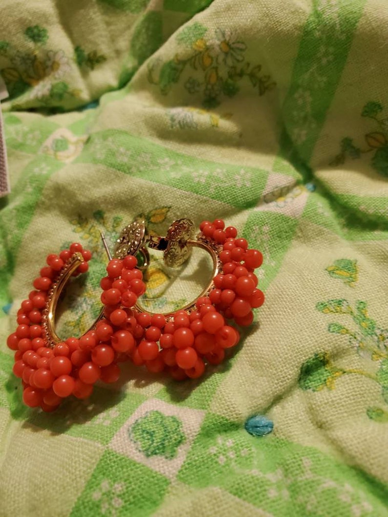 May include: A pair of hoop earrings with a gold base and red beads. The beads are clustered together to create a textured look.
